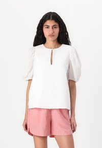 Haut blanc texturé avec des manches bouffantes et un d�écolleté en forme de serrure, associé à un short rayé rouge et blanc.
