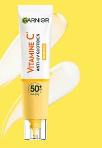 Tube de crème solaire avec un corps blanc et une base jaune, présentant un texte vert et orange. Contient un SPF 50+, avec un capuchon à buse transparent et une texture crémeuse.