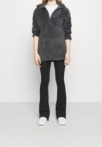 Sudadera de forro polar gris con medio cierre, tela texturizada y mangas remangadas, combinada con pantalones ajustados negros y zapatillas blancas.