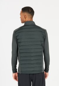 Grå isoleret vest med en glat stoffront og en tekstureret quiltet ryg, med en høj krave og tætsiddende lange ærmer.