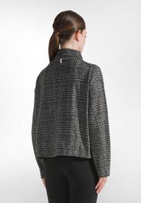 Svart och vit mönstrad jacka med hög krage och kort passform. Texturerat tyg med en liten rosa logotyp på baksidan av nacköppningen.