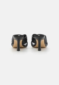 Chaussures à talons hauts noires au design épuré, fabriquées en matériau texturé noir avec des détails transparents à l'arrière. Semelle en caoutchouc avec un talon carré.