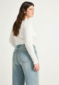 Maglietta bianca a maniche lunghe a coste abbinata a jeans azzurri a vita alta. I jeans presentano un fit rilassato e due tasche posteriori.