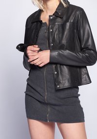 Zwarte leren jack met een kraag, drukknoopsluitingen en een voorzak. Slank passend grijs geribbeld kleed met een centrale ritsdetail.