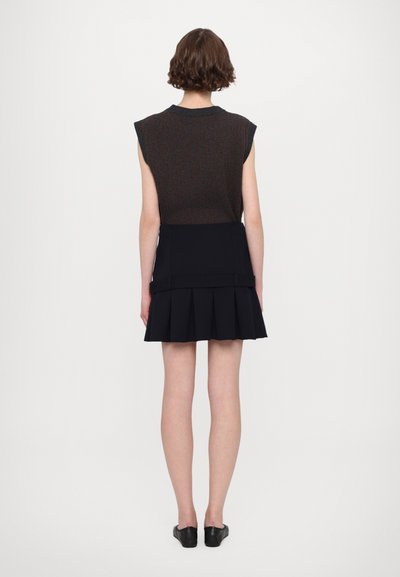 Falda negra plisada con cintura ajustada, combinada con una blusa sin mangas de patrón oscuro. Textura suave, diseño minimalista.