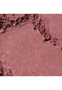 Maquillage en poudre mauve scintillant, légèrement texturé avec des zones de surface lisse et des bords rugueux et brisés, vu en gros plan.