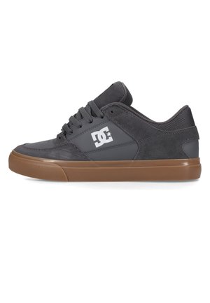 Donkergrijze lage skate schoen met bruine rubberen zool, zwarte veters en wit DC-logo op het zijpaneel.