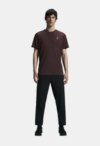 T-shirt bordeaux à manches courtes avec col rond et détails de logo, associé à un pantalon noir ample et des chaussures de sport noires.