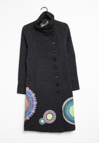 Cappotto nero con texture, colletto alto e fila asimmetrica di bottoni, decorato con motivi circolari colorati vicino all'orlo.