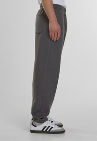 Pantalones de chándal grises con cintura elástica y bolsillo lateral, con un diseño de pierna recta y tejido suave, combinados con zapatillas blancas y negras.