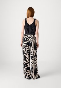 Black sleeveless top with ruffled edges paired with black and beige patterned wide-leg pants featuring a leaf design. Flat footwear.