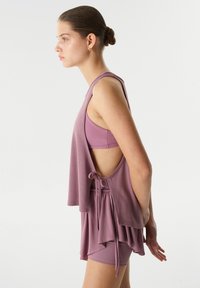 Conjunto de ropa deportiva en color lavanda que incluye una camiseta sin mangas con la espalda descubierta y un detalle de lazo, acompañado de unos pantalones cortos ajustados a juego. Textura suave.