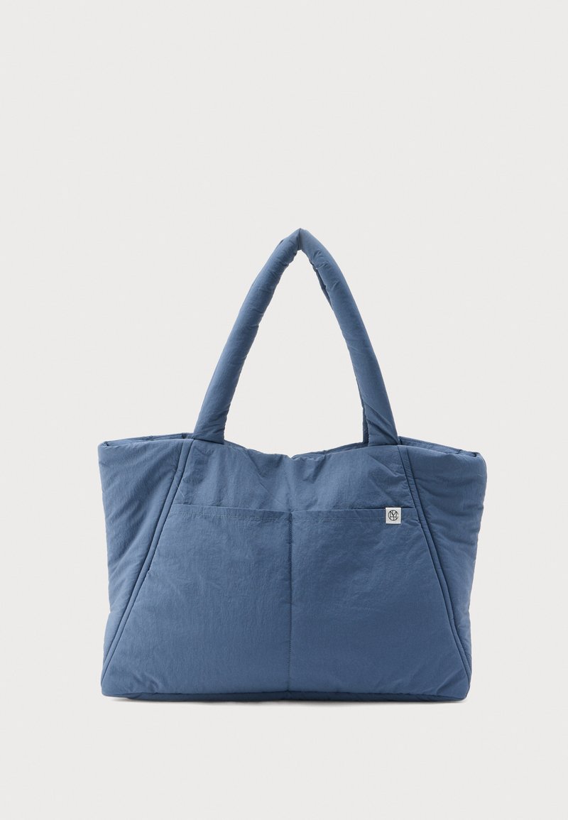 Τσάντα tote από μπλε υφασμάτινο ύφασμα, με διπλές λαβές, μεγάλη ορθογώνια μορφή, με μπροστινή τσέπη και λεπτομέρεια λογότυπου στο πλάι.