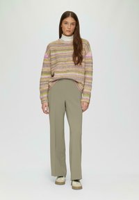 Gehaakte pastelgestreepte trui met een relaxed fit, gecombineerd met hooggewaisted kaki broeken en beige sneakers, staande tegen een neutrale achtergrond.