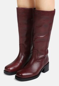 Botas de couro bordô até ao joelho com um acabamento elegante, salto robusto e um design de costura subtil na parte da perna.