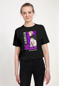 Czarny bawełniany t-shirt z charakterystyczną postacią i napisem w różowym i białym kolorze, umieszczony na purpurowym tle w geometrze.