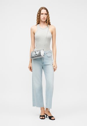 Γυναίκα που φορά γκρι αμάνικο τοπ, ανοιχτό μπλε τζιν με φθαρμένα τελειώματα, μαύρα πέδιλα με τακούνι, κρατώντας ασημένια τσάντα χιαστί με τρουκς και σχέδιο καρδιάς.