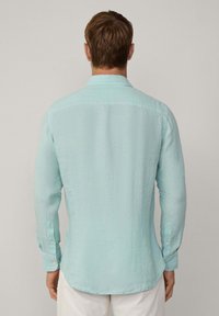 Lichtblauwe blouse met lange mouwen van gekreukt materiaal, met een standaard kraag, knoopmanchetten en een afgeronde zoom. Eenvoudig en strak ontwerp.