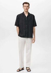 Korte mouwen zwart-wit gestreepte shirt, lichte broek en zwarte sandalen. Casual pasvorm, knoopsluiting aan de voorkant, zachte stof en ontspannen ontwerp.