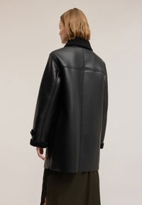 Giacca in pelle nera con design doppiopetto, colletto nero morbido e polsini testurizzati, con vestibilità comoda e finitura liscia.