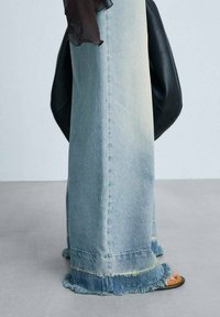 Light blue denim wide-leg jeans with frayed hems, featuring a slight fade and visible stitching. Paired with black sandals.