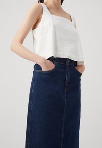 Vit linne kort topp med breda axelband, kombinerad med en mörk denimkjol med hög midja och framfickor. Texturerad tyg, rena linjer.