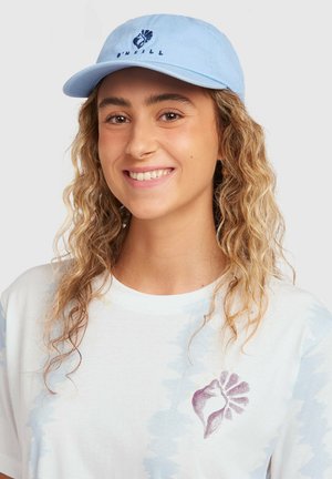 Svetlo modra baseball kapa s ukrivljenim robom in vezenim logotipom v temno modri barvi. Združena z belo majico s subtilnim modrim vzorcem.