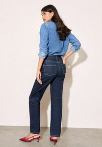 Svijetloplava traper košulja s gumbima, uparena s tamnoplavo visokim trapericama koje imaju stražnje džepove i kontrastnu šav.