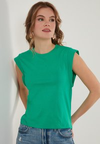 T-shirt verde a maniche corte con colletto tondo e vestibilità rilassata, realizzato in tessuto liscio; abbinato a pantaloni corti in denim strappato.