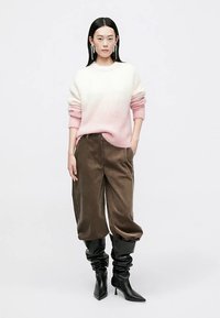 Kampsun kreemikast roosani gradientsetes toonides, kombineeritud lahtiste pruunide trikotaaždresside ja mustade kontsakingadega, mis ulatuvad põlveni ja on lõdvalt istuvad.