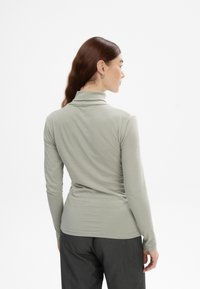 Langärmeliger, enganliegender Rollkragenpullover aus hellgrauem Stoff mit glatter Textur und minimalistischem Design, kombiniert mit dunkelgrauen Hosen.