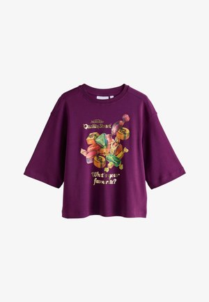 Violeta īsām piedurknēm kreklit, kas rotāts ar konfekšu grafiku un tekstu: "Kāds ir tavs mīļākais?" zeltainā krāsā. Mīksts audums un brīvs griezums.