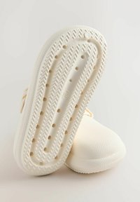 Licht crèmekleurig schoeisel met een gestructureerd bovenwerk, rubberen zool met een visgraatpatroon en geventileerde gaatjes voor ademend vermogen.