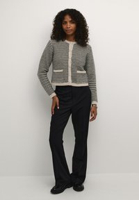 Knitted cardigan in black and beige check pattern, featuring a round neck, button closure, two front pockets, and ribbed cuffs.