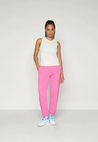 Top sin mangas blanco combinado con pantalones de chándal rosa brillante. Calzado blanco con acentos azules. Diseño simple con un corte relajado.