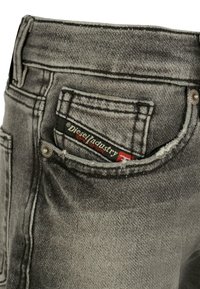Jeans in denim grigio con una finitura sbiadita, caratterizzati da dettagli di cucitura, una tasca posteriore con un'etichetta rossa e nera e una chiusura a bottone.