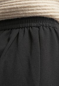 Musta kudottu kangas, jossa on pehmeä rakenne, elastisella vyötäröllä ja rypytetyt yksityiskohdat vyötäröllä. Yllä kerma beige ribattua neulekangasta.