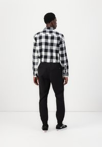 Langarm zwart-wit geblokt shirt met knoopmanchetten, gecombineerd met zwarte, taps toelopende broek en zwarte sneakers. Achteraanzicht, effen achtergrond.