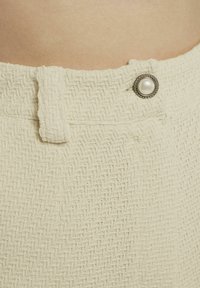 Crème gekleurde shorts met een geweven patroon, voorzien van een parelknopaccent op de taille. Het ontwerp bevat een veilige sluiting.