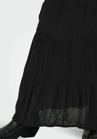 Robe noire à volants en tissu léger, ornée de broderies florales au bord et associée à des bottes de cowboy noires.