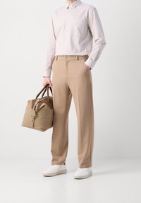 Beiget väriset housut yhdistettynä vaaleaan raidalliseen paitaan ja valkoisiin tennareihin. Kädessä ruskea ja beige nahkalaukku, jossa vetoketjusuljin.