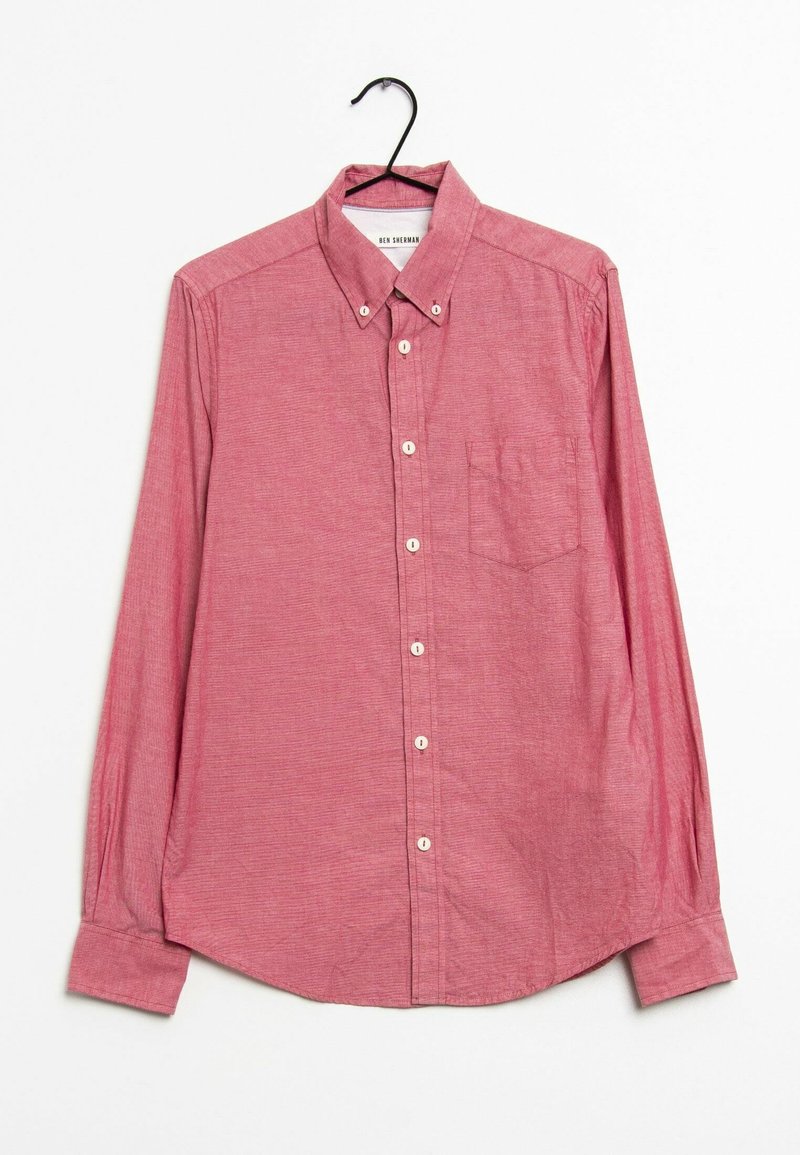 Chemise rouge à manches longues avec boutons et poche poitrine suspendue sur un cintre noir devant un fond blanc.