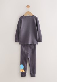 Ensemble pour enfants composé d'un haut à manches longues et d'un pantalon gris foncé suspendu sur un cintre en bois, avec un motif coloré de chien sur le bas de la jambe du pantalon.