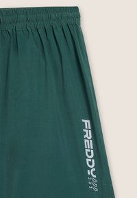 Pantalones cortos deportivos verdes con una cinturilla elástica. Presentan el logo blanco "FREDDY" impreso verticalmente en un lado. Tejido suave y ligero.