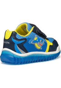 Baskets pour enfants bleues avec un design de requin, dotées d'une sangle Velcro, d'accents jaunes et d'une semelle en caoutchouc texturée.
