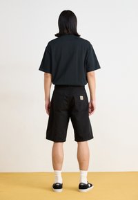 Black short-sleeve t-shirt paired with black shorts. Smooth fabric; relaxed fit; shorts feature back pockets and a small logo patch.
