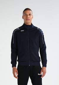 Marine atletiekjack met witte accenten, ritssluiting, hoge kraag en logo's op de borst en schouders. Glad, lichtgewicht stof.
