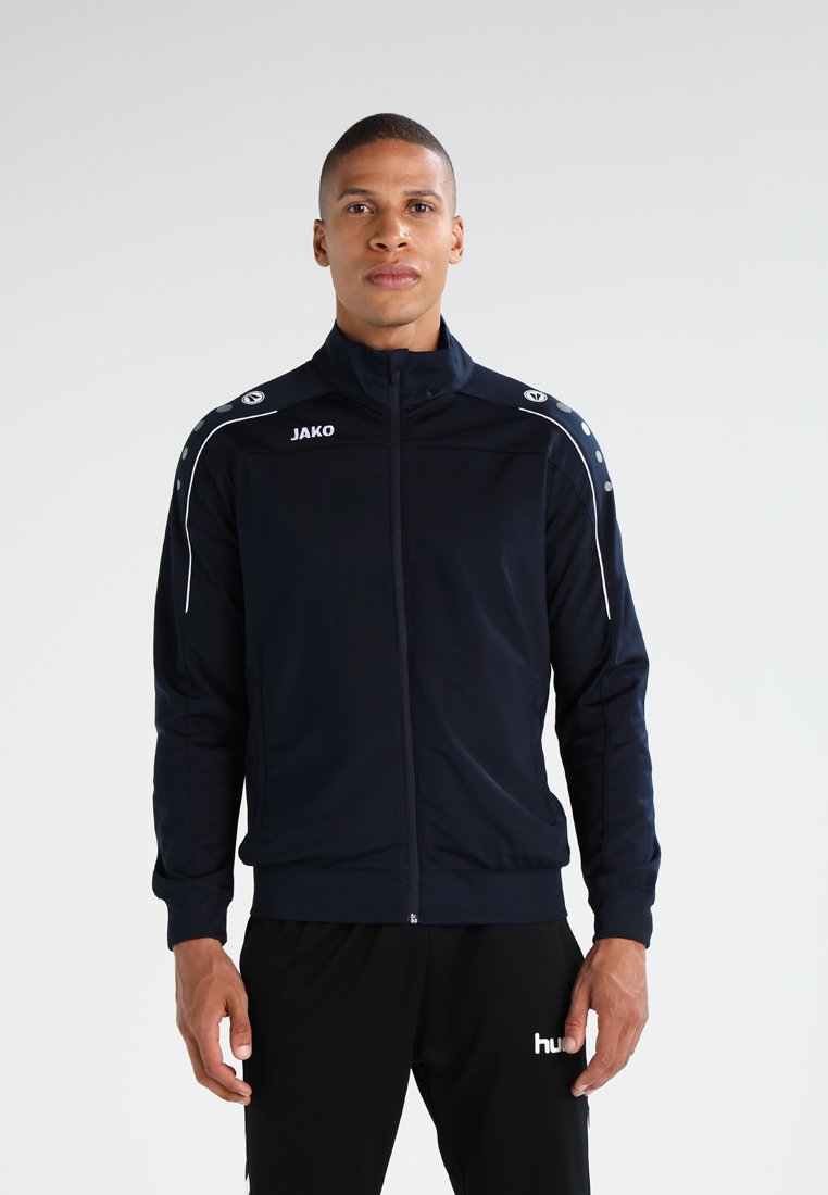 Marine atletiekjack met witte accenten, ritssluiting, hoge kraag en logo's op de borst en schouders. Glad, lichtgewicht stof.