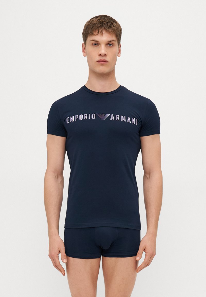 T-shirt ajustado azul marinho com o logotipo "Emporio Armani" em roxo, com mangas curtas e decote redondo, emparelhado com calções combinando.