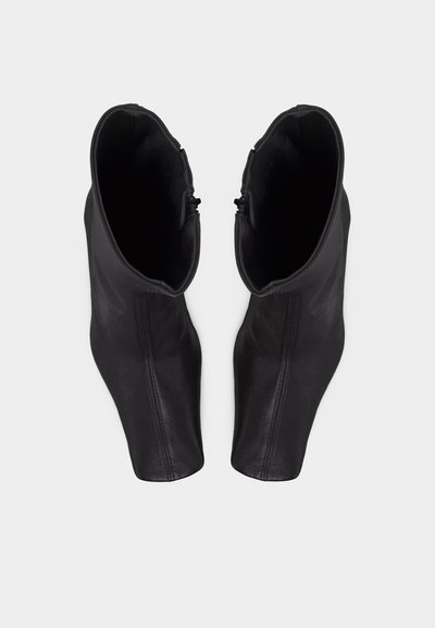 Ζευγάρι μαύρων μποτών αστραγάλου με φερμουάρ στο πλάι και μυτερά δάχτυλα, φωτογραφημένα από πάνω σε λευκό φόντο.